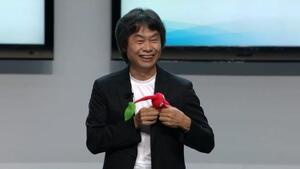 Miyamoto Hints At Pikmin 4 / Shigeru Miyamoto on stage wearing a dark jacket and white T-shirt and holding a red Pikmin plushie. / Image credit: BagoGames / This work is licensed under Creative Commons Attribution 2.0